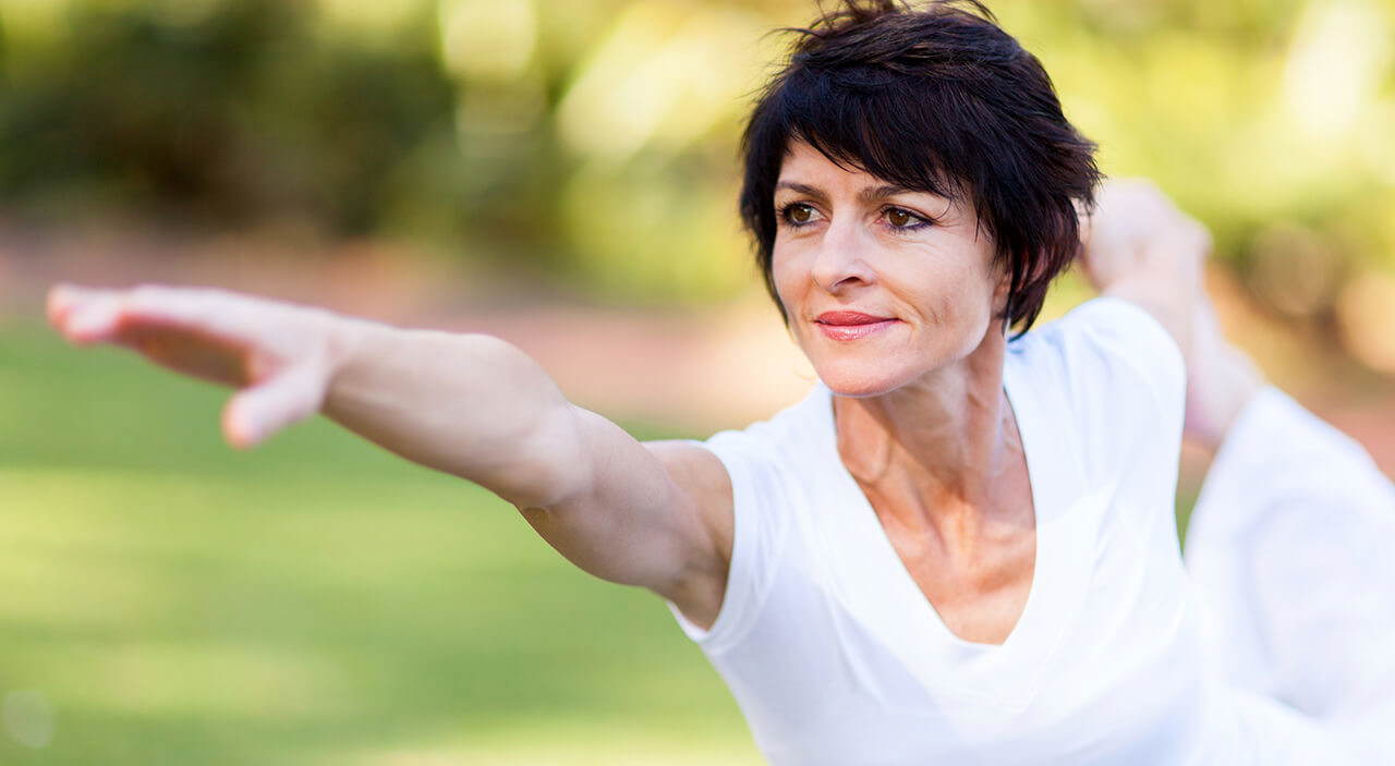 Active older woman holding a yoga pose, feeling youthful after fat grafting.
