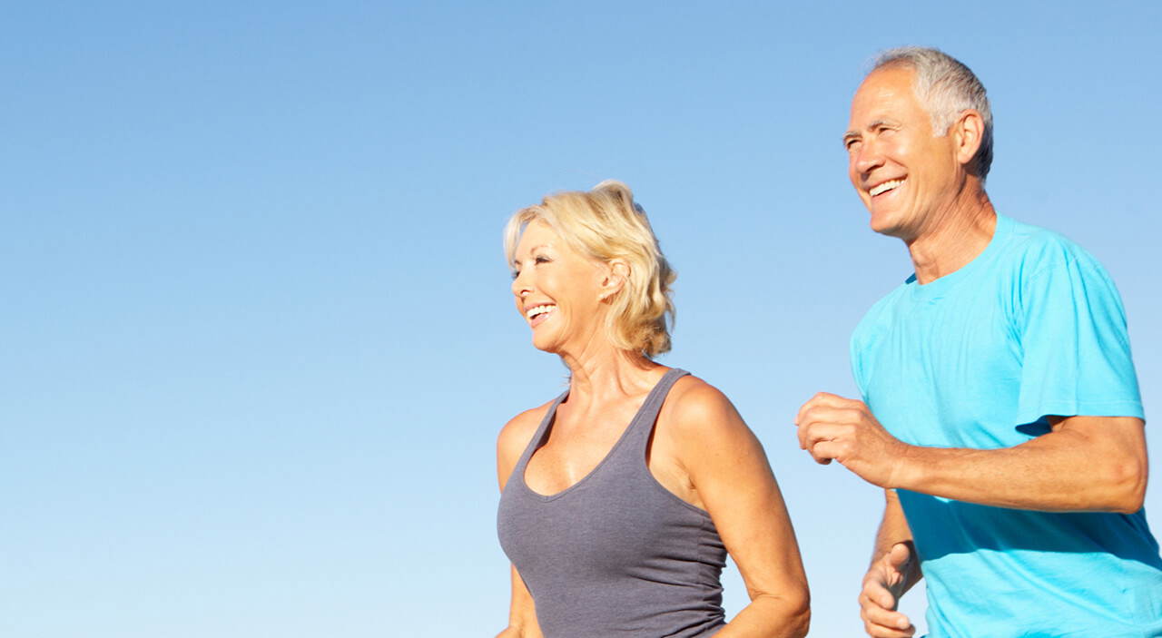 Active couple jogging on the beach, looking youthful and refreshed.