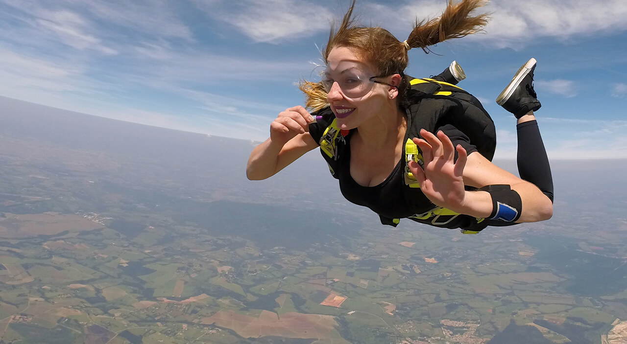 Confident woman skydiving and smiling, feeling free after breast augmentation and lift.