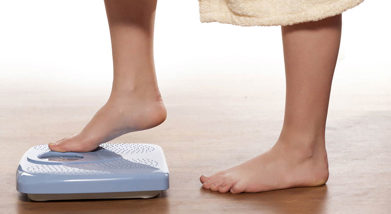 Woman stepping on a scale, monitoring her weight and body composition.