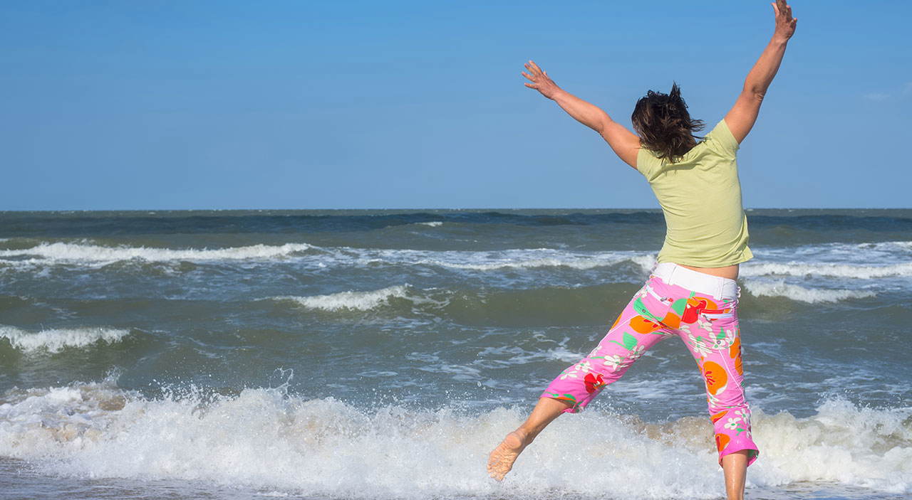 Happy woman jumping for joy at the beach after her transformation.
