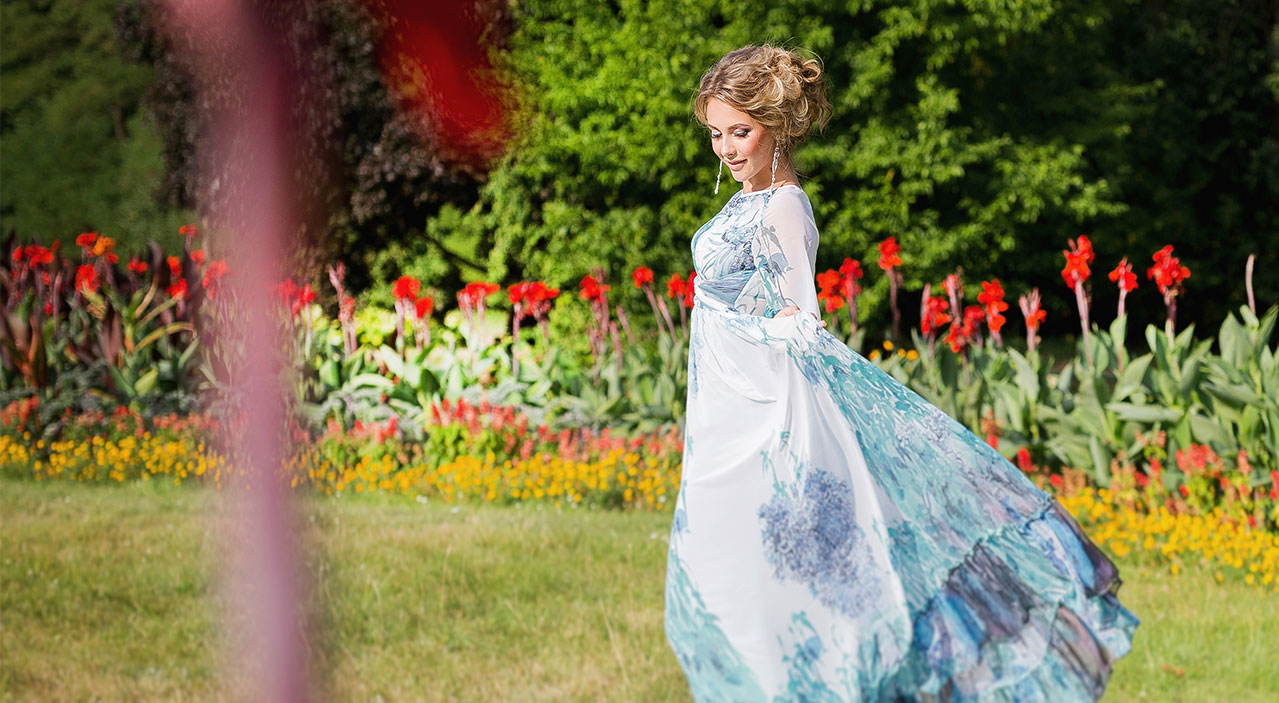 Young woman in flowing dress standing in a garden with flowers.