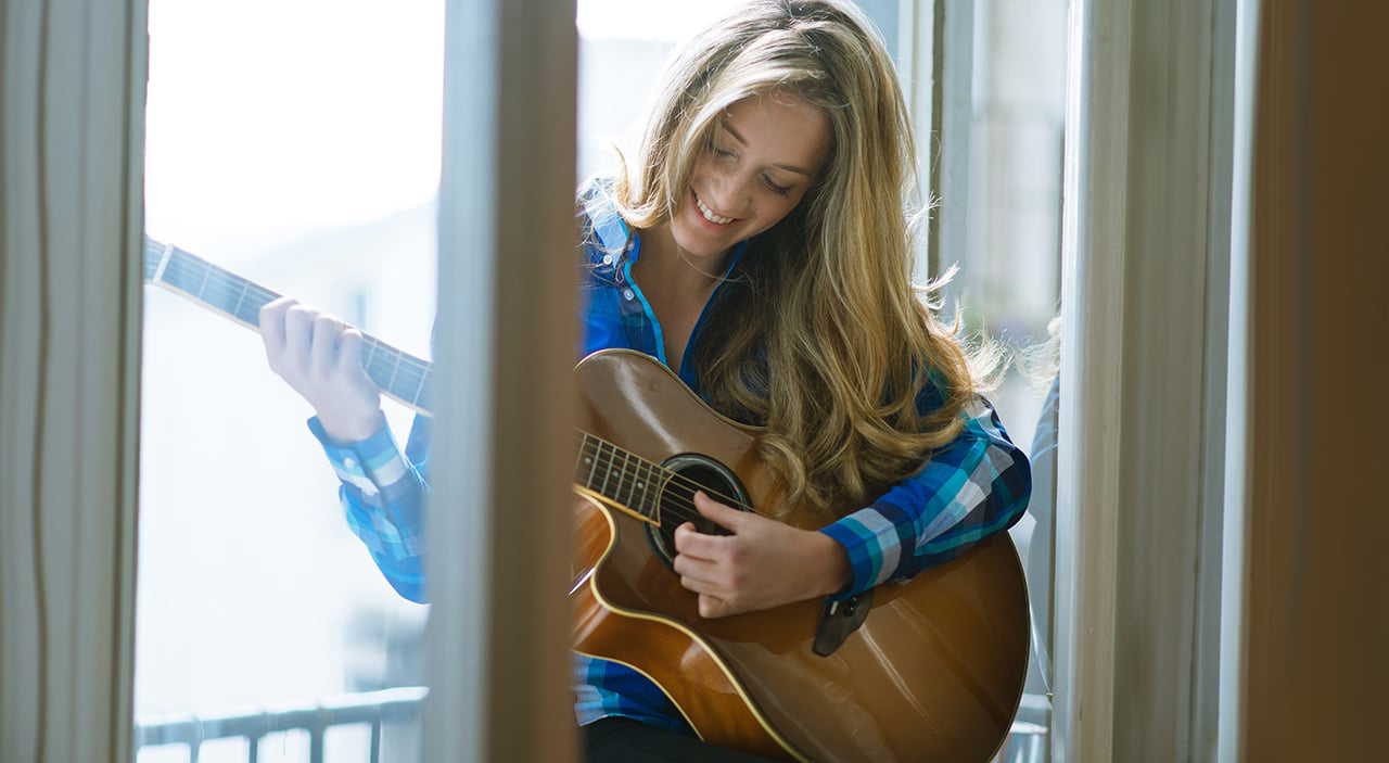 Woman relaxing by the window playing guitar, feeling at ease.