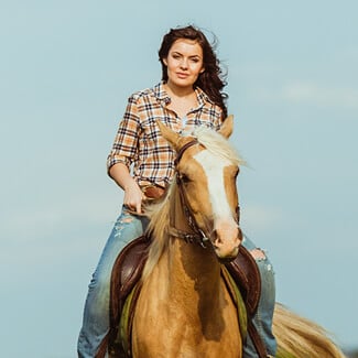 Woman and man riding horses in grassy field.