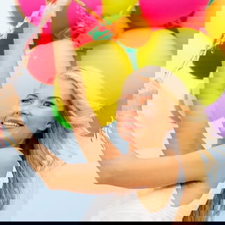 Woman holding a bunch of colourful balloons against a blue skin.