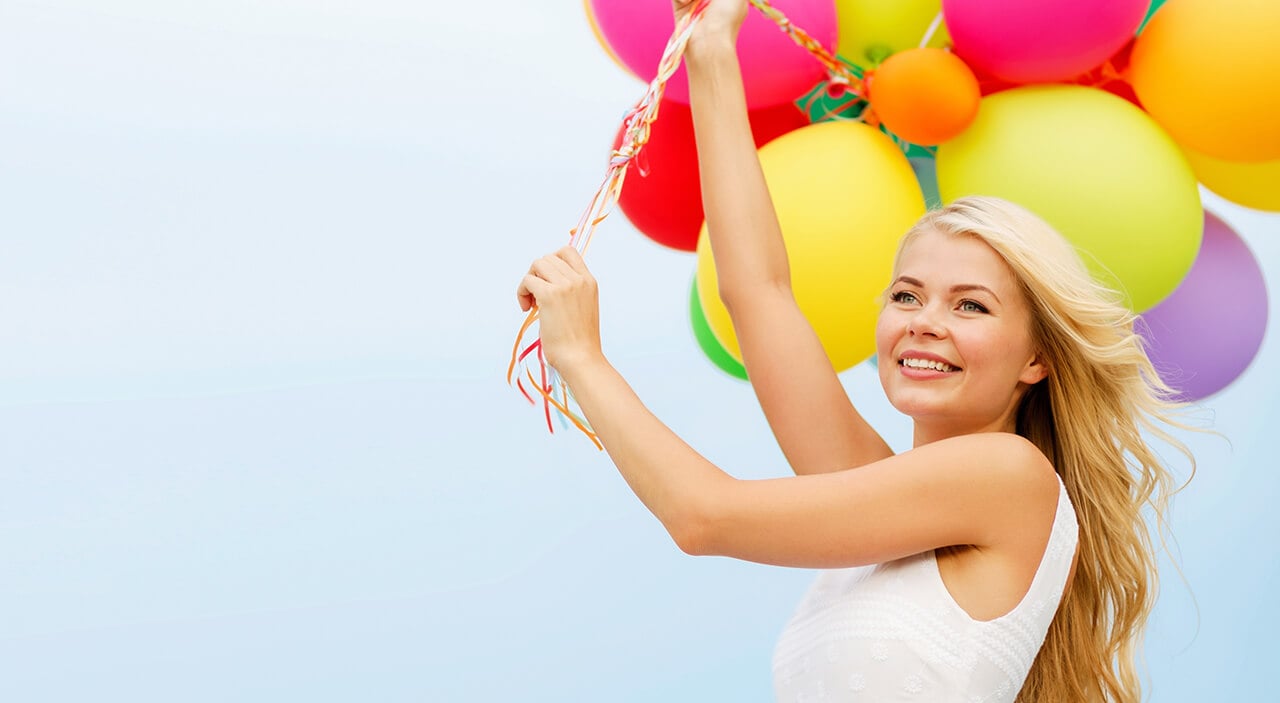 Woman holding a bunch of colourful balloons against a blue skin.