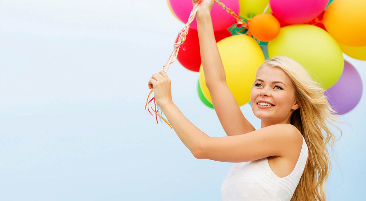Woman holding colourful balloons against a blue sky.