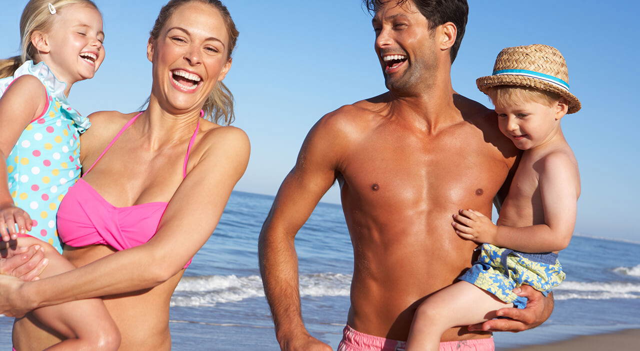 Laughing woman with daughter, husband and son at the beach.