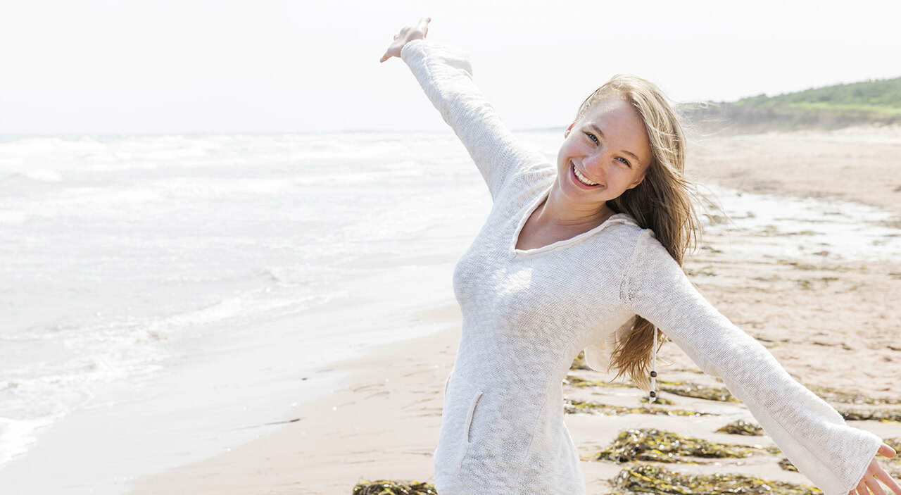 Young woman smiling with arms outstretched on the beach.