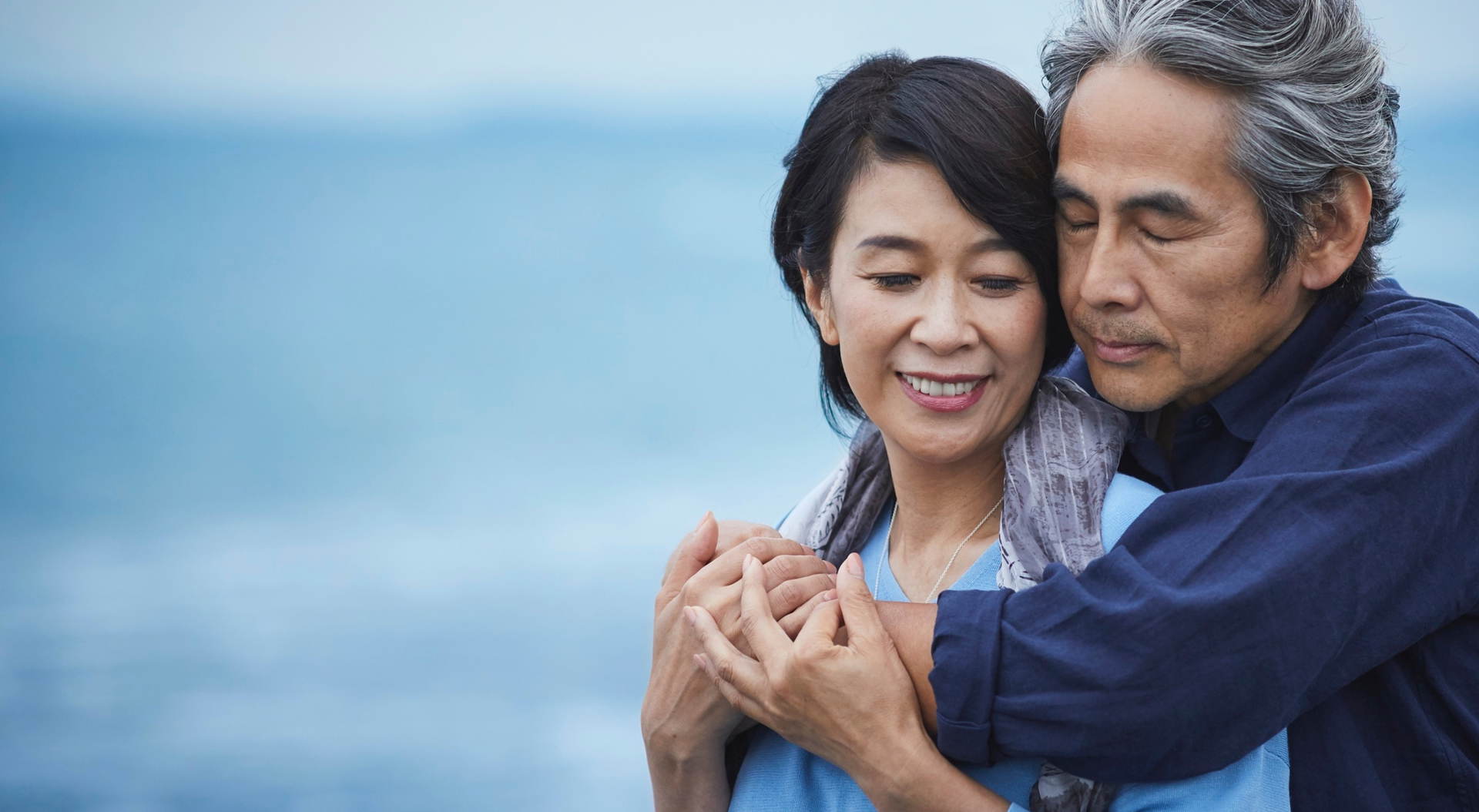 Radiant older woman smiling at her husband on the beach, looking naturally youthful.