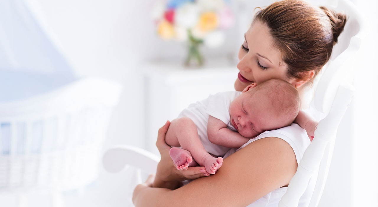 New mother sitting with baby in her arms, considering a tummy tuck after pregnancy.